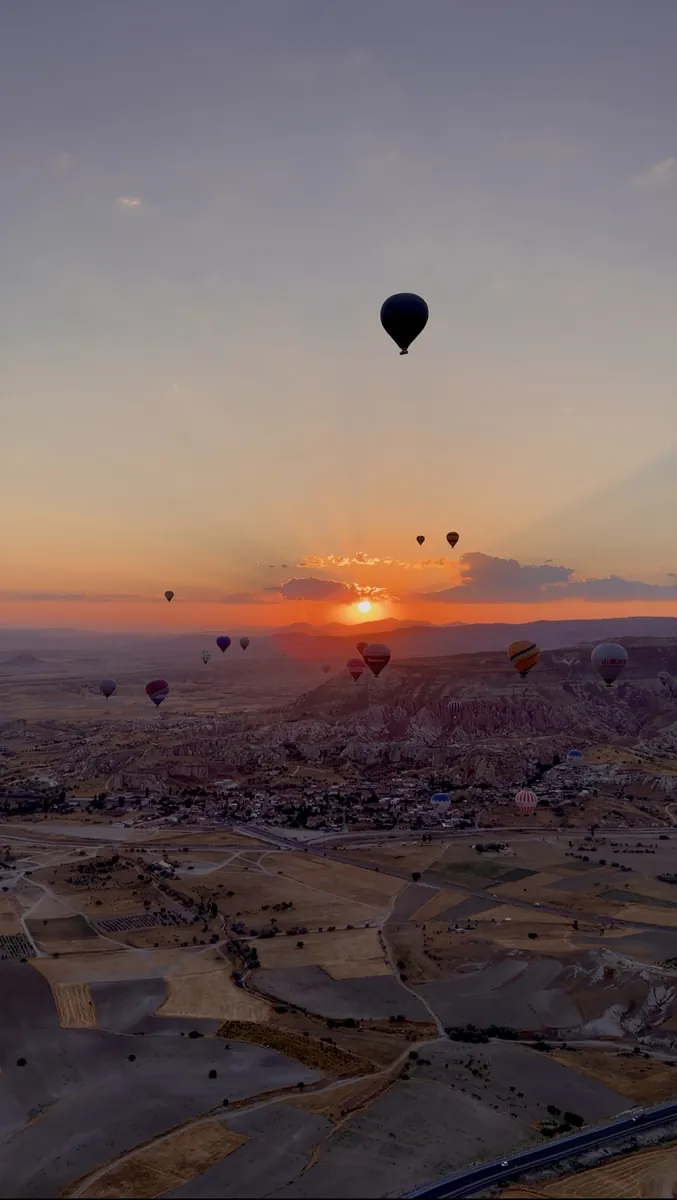La silueta de un globo aerostático con un dramático rayo de sol entre las nubes