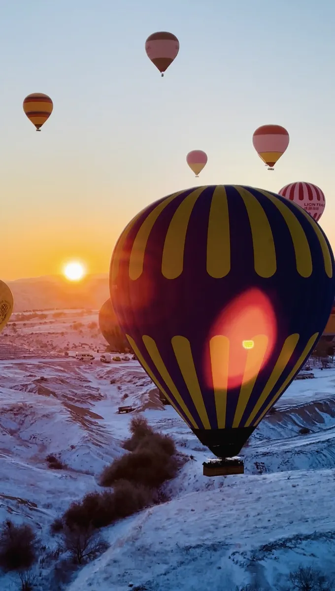 A hot air balloon glowing with burner flame against the Cappadocia sunrise